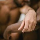 Close-up of two shirtless men embracing with focus on hand, conveying intimacy.