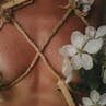 Aesthetic nude featuring delicate flowers intertwined with rope for a conceptual art piece.